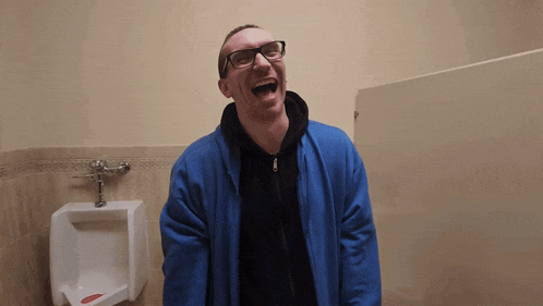 a man wearing glasses and a blue jacket is laughing in a bathroom stall