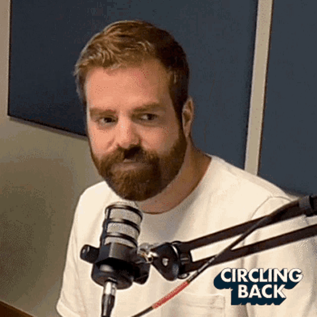 a man with a beard is sitting in front of a microphone with the words circling back on the bottom right