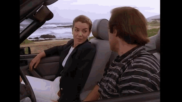 a man and a woman are sitting in a car looking at each other