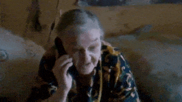 an elderly woman is talking on a cell phone while sitting on a bed .
