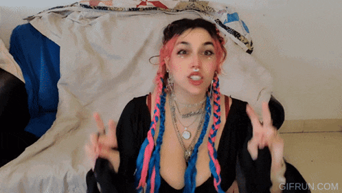 a woman with pink and blue braids is sitting on a couch with a gifrun.com logo in the corner