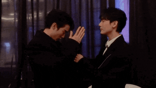 two men are standing next to each other with their hands folded in front of their faces .