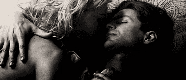 a black and white photo of a man and woman hugging each other in bed .