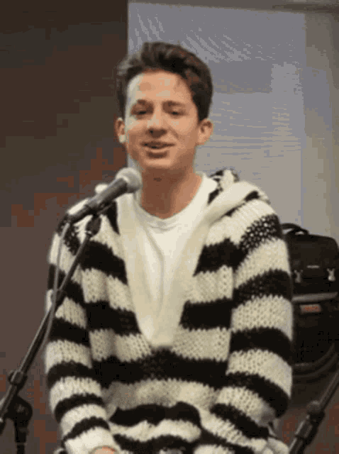 a man wearing a black and white striped sweater is sitting in front of a microphone