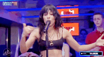 a woman singing into a microphone in front of a crowd with cruel tv in the background