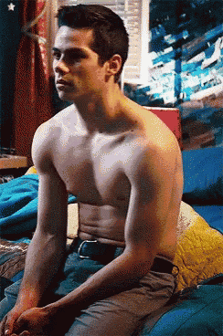 a shirtless man is sitting on a bed in front of a window