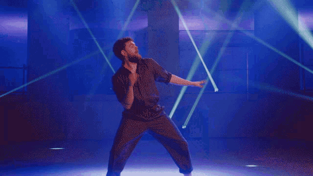 a man in a black shirt is dancing in front of purple lights