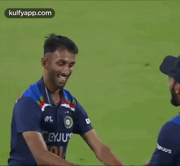 two cricket players are shaking hands on the field .