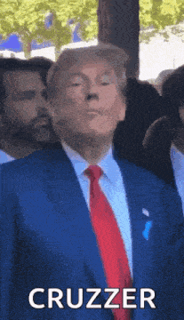 donald trump is wearing a blue suit and red tie and making a funny face while standing in front of a crowd .