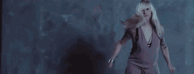 a woman in a purple dress is holding a knife in front of a wall with blood on it .