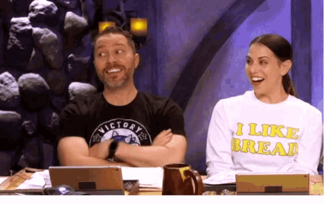 a man wearing a victory shirt sits next to a woman wearing a sweater that says i like bread