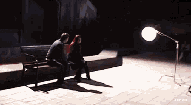 a man and a woman sit on a bench in the dark with a red gif behind them