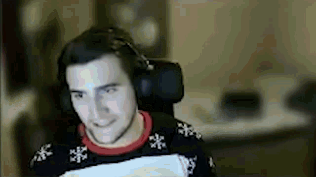 a man wearing headphones and a christmas sweater is sitting in a chair .