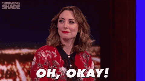 a woman in a red jacket is sitting on a stage with the words `` oh , okay '' written on the screen .