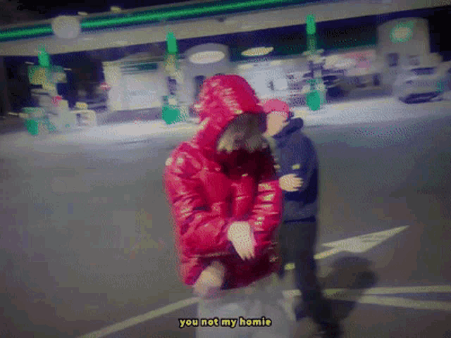 a man in a red jacket is standing in front of a gas station and says you not my homie
