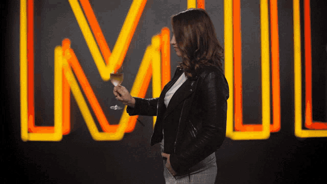 a woman holds a glass of wine in front of a neon sign that says ln