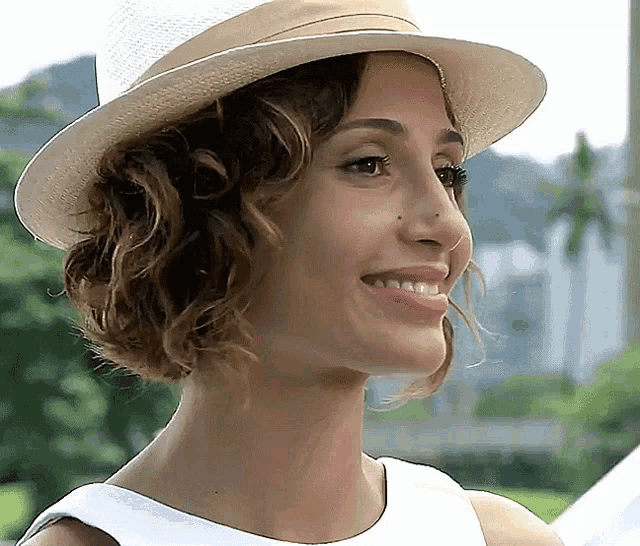 a woman wearing a hat and a white dress smiles for the camera