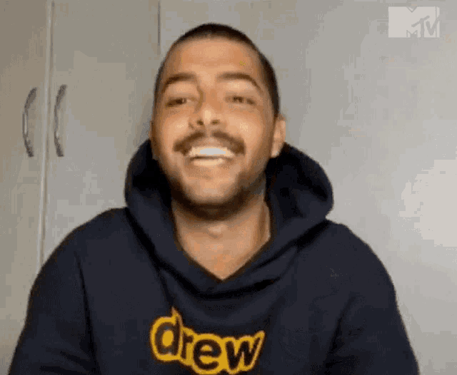 a man wearing a drew hoodie is smiling and looking at the camera .