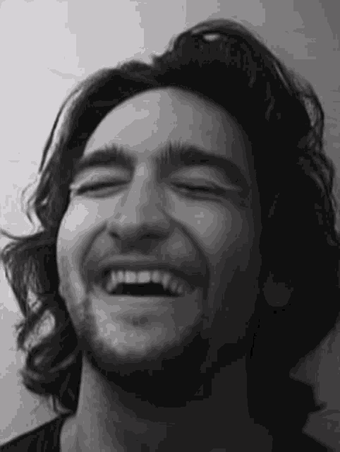 a man with long hair and a beard is laughing with his eyes closed