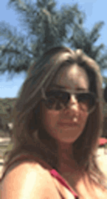 a woman wearing sunglasses is standing in front of a palm tree in a blurry photo .