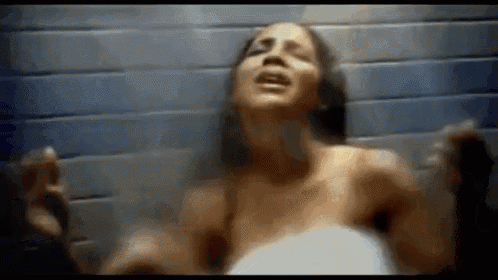 a naked woman is standing in front of a blue brick wall .