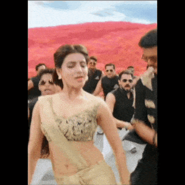 a woman in a gold saree is dancing in front of a group of men .