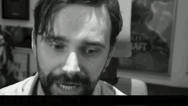 a black and white photo of a man with a beard sitting in a chair .