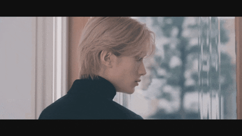 a man in a black turtleneck stands in front of a window