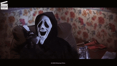 a person in a scream mask is sitting on a couch talking on a phone