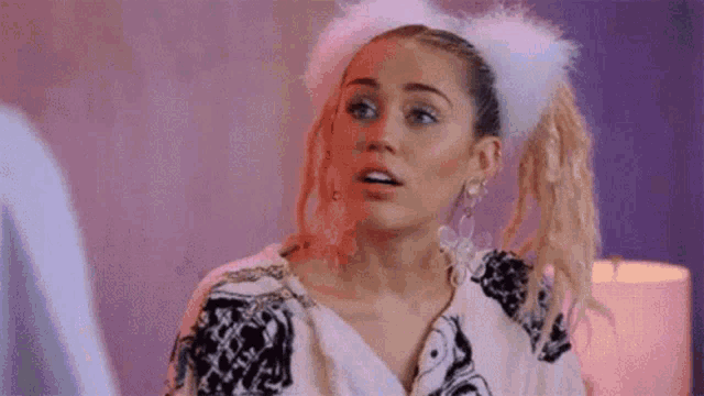 a woman wearing a furry headband and earrings is making a surprised face .