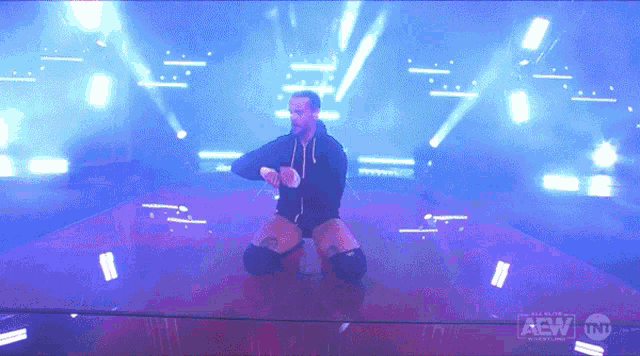 a wrestler is kneeling on a stage with aew written on the bottom