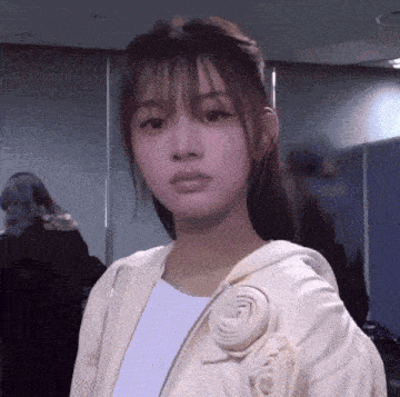 a woman wearing a white jacket with a flower on it looks at the camera .
