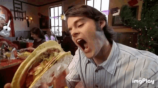 a man in a striped shirt is eating a taco with his mouth wide open ..