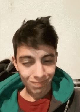 a young man wearing a green hoodie and a red t-shirt is making a funny face .