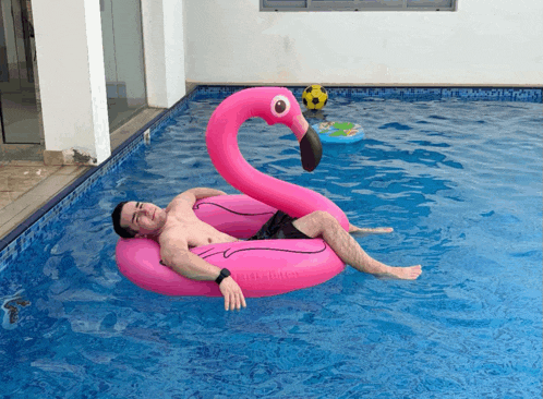 a man is floating on a pink flamingo float in a pool
