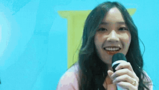 a young woman is smiling while holding a microphone in front of a blue wall .