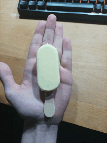 a hand holding a yellow ice cream bar with a wooden stick