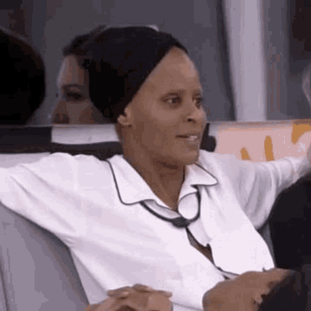 a woman in a white shirt and black hat is sitting on a couch with her arms outstretched .