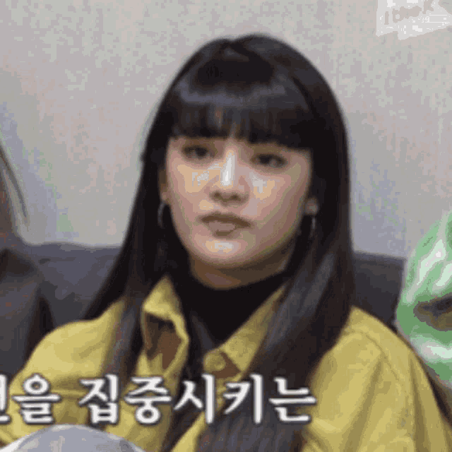 a woman in a yellow jacket is sitting on a couch with foreign writing on the wall behind her