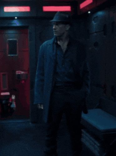 a man wearing a hat and a coat is standing in a dark room