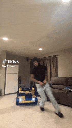a man is dancing in a living room with a toy car in the background .