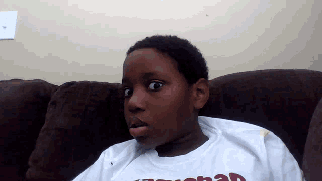 a young boy sitting on a couch wearing a t-shirt that says ' jesus ' on the front