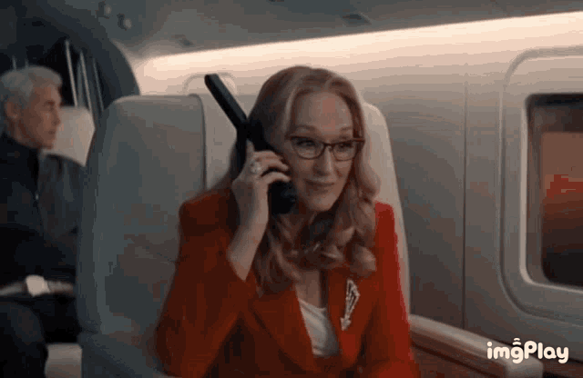 a woman in a red suit is talking on a cell phone on a plane
