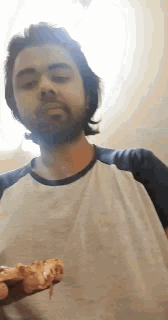 a man with a beard is holding a slice of pizza in front of his face .