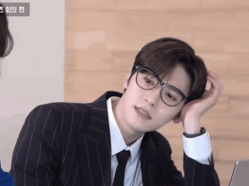 a man wearing glasses and a suit has his hand on his chin