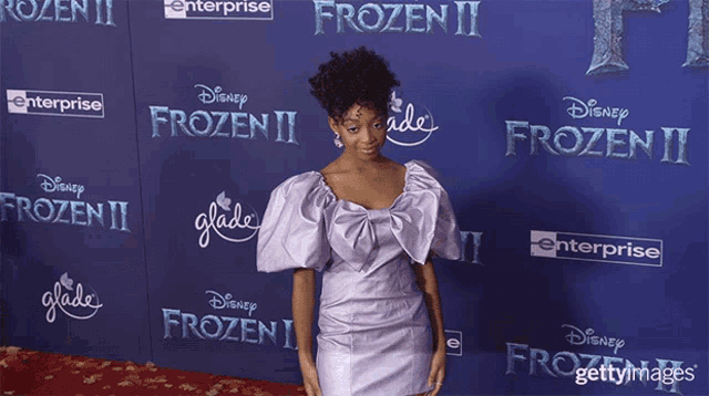 a woman in a purple dress is standing in front of a disney frozen ii poster