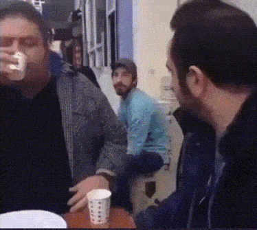 a man drinking from a cup while another man sits on a chair