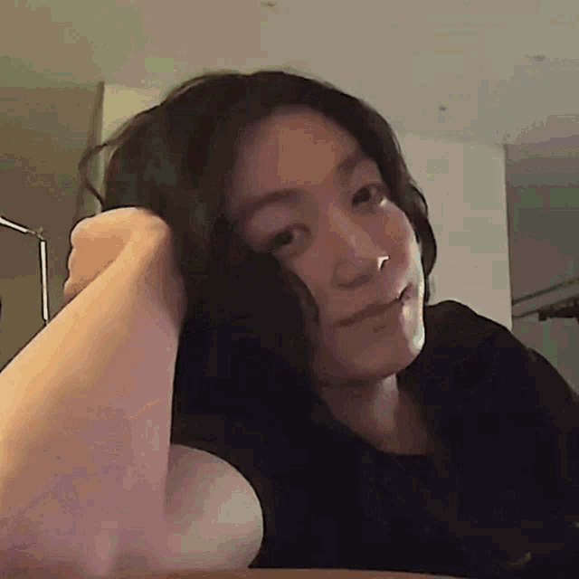 a woman with long dark hair is sitting at a table with her hand on her head .