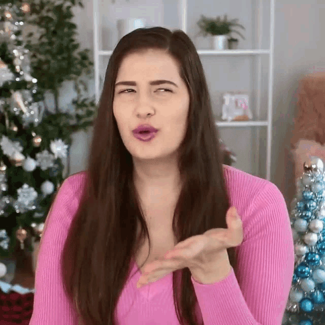 a woman in a pink sweater is blowing a kiss