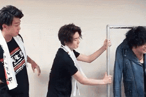 three men are standing next to each other in a room . one of the men is holding a hanger .